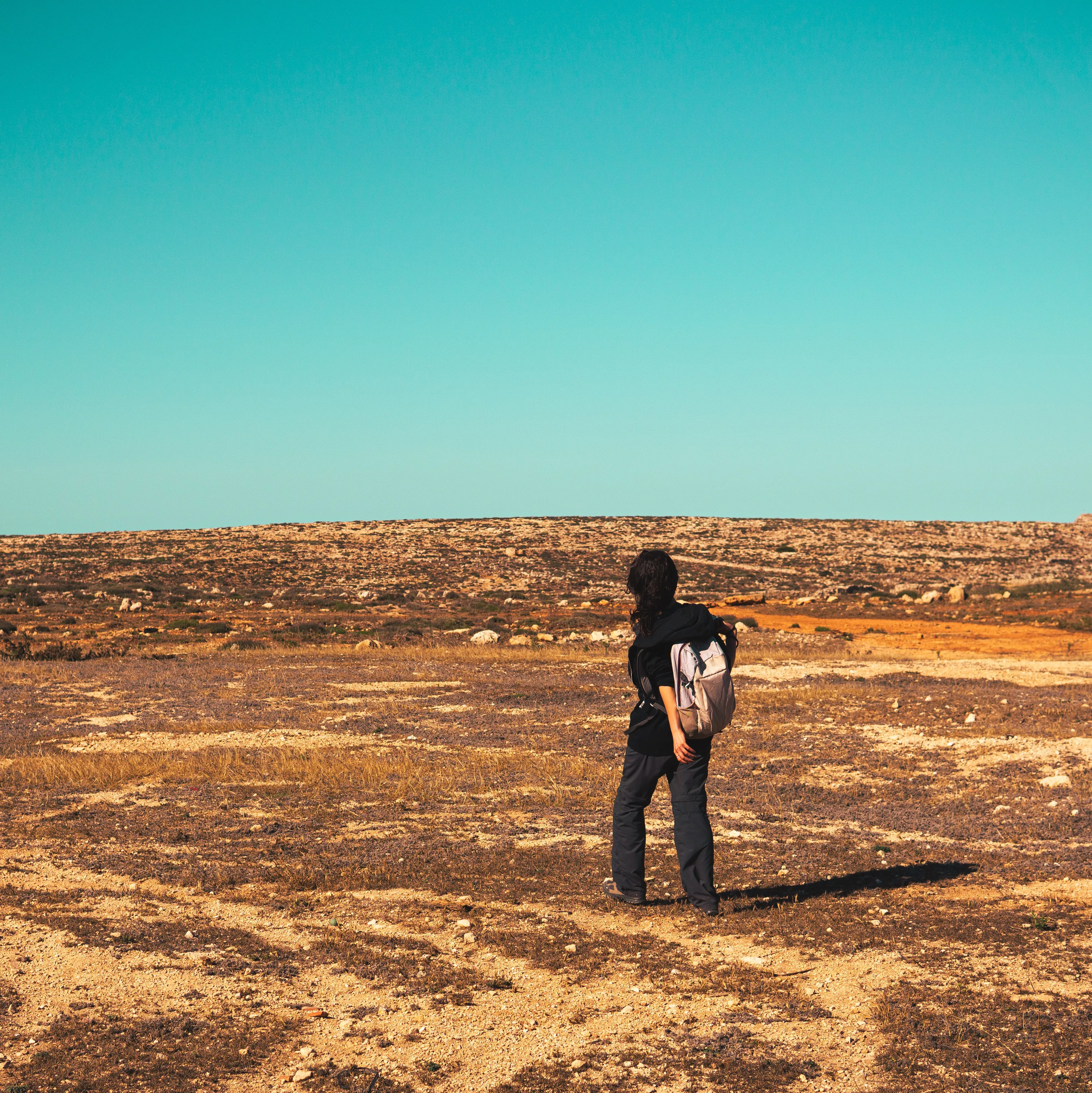 Person walking across a dry landscape beneath a blue sky